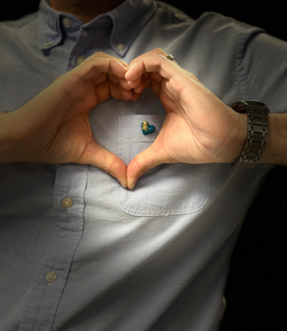 Hands making a heart shape over a blue heart pin